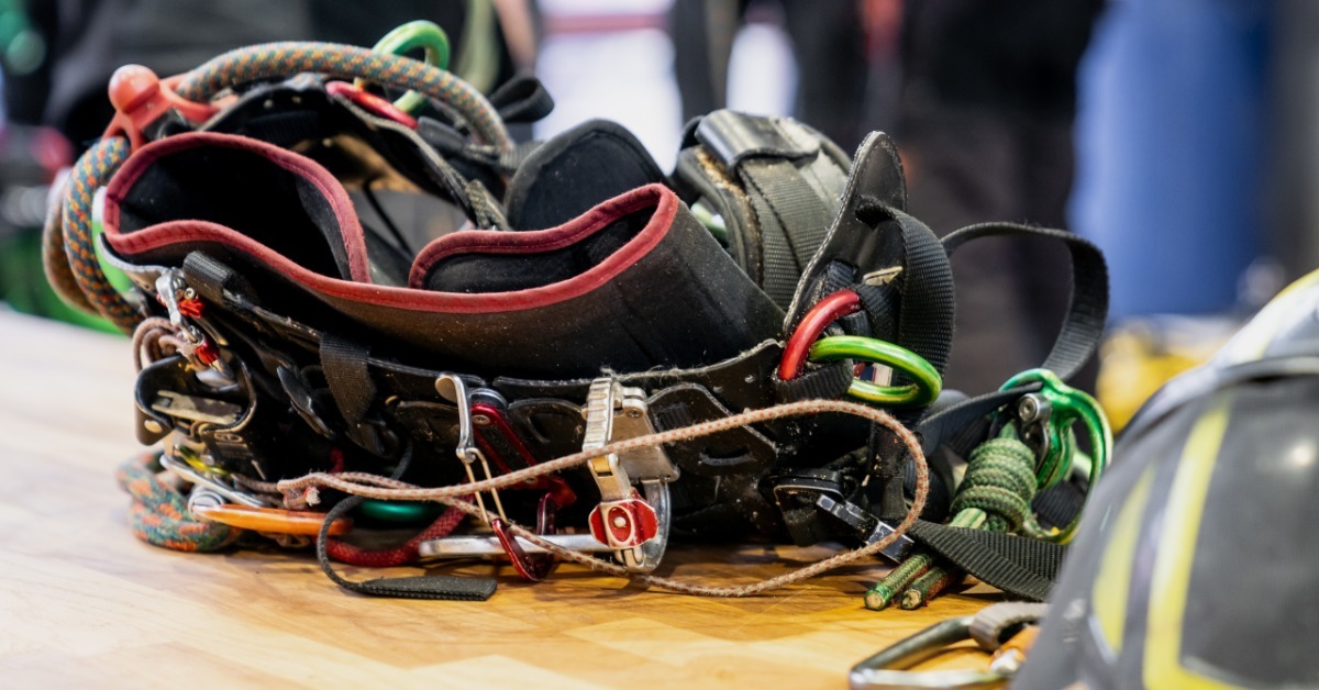 A close-up of a safety helmet and a tree climbing harness with various accessories attached set up on a table.