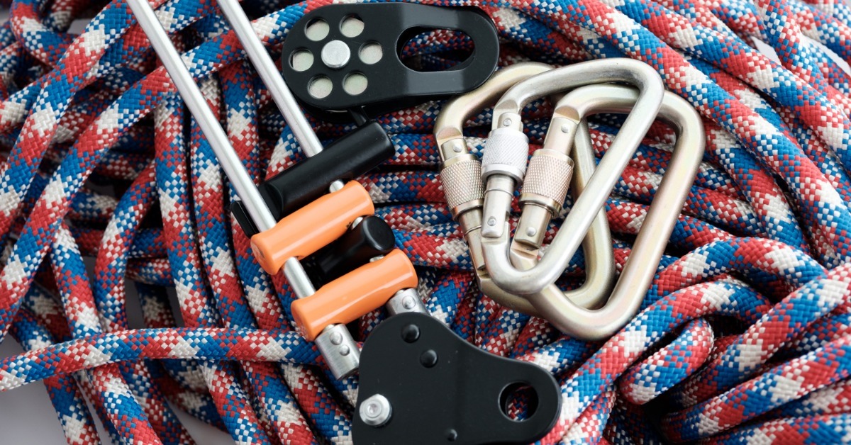 A coil of red, white, and blue climbing rope with silver carabiners, black pulleys, and orange-handled climbing hardware.