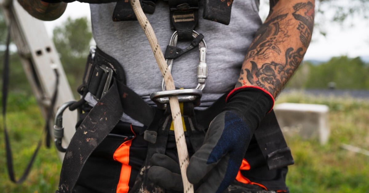 An arborist wearing black gloves while threading a rope through the carabiner attached to their belt.