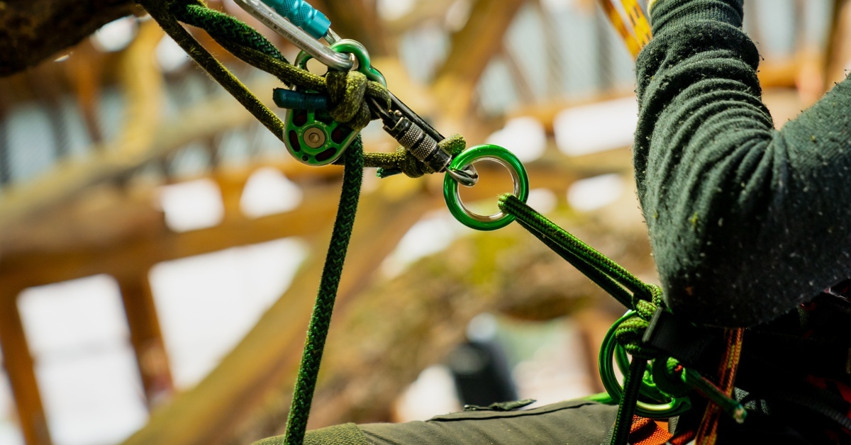 A person attached to a system of pulleys, ropes, and carabiners. They are inside a large unfinished structure.