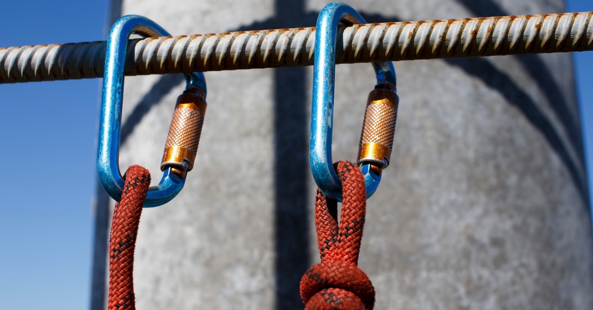 A metal bar oriented horizontally with two clips attached to it. Each clip has a knot tied around it.