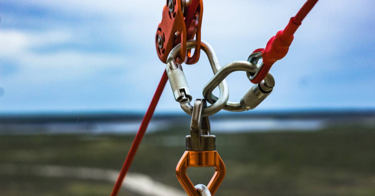 Multiple carabiners and connectors attached to a red pulley. The pulley and carabiners are connecting two red ropes.