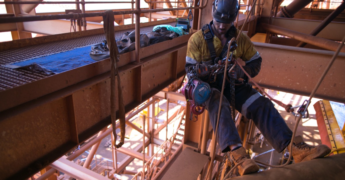 A worker in a hard hat wearing a harness with ropes and various components attached within a large metal structure.