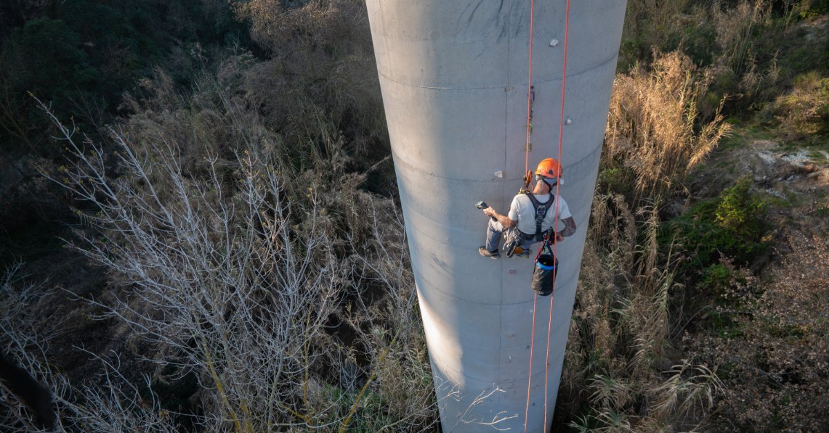 A person wearing an orange safety helmet and a harness connected to a rope while working on a tall concrete structure.