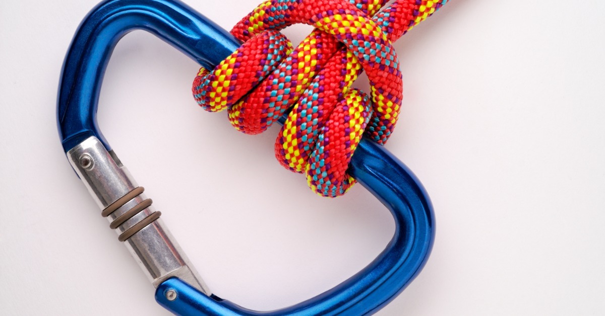 A close-up of a red climbing rope with blue, yellow, and purple stripes attached to a blue carabiner with a Prusik knot.