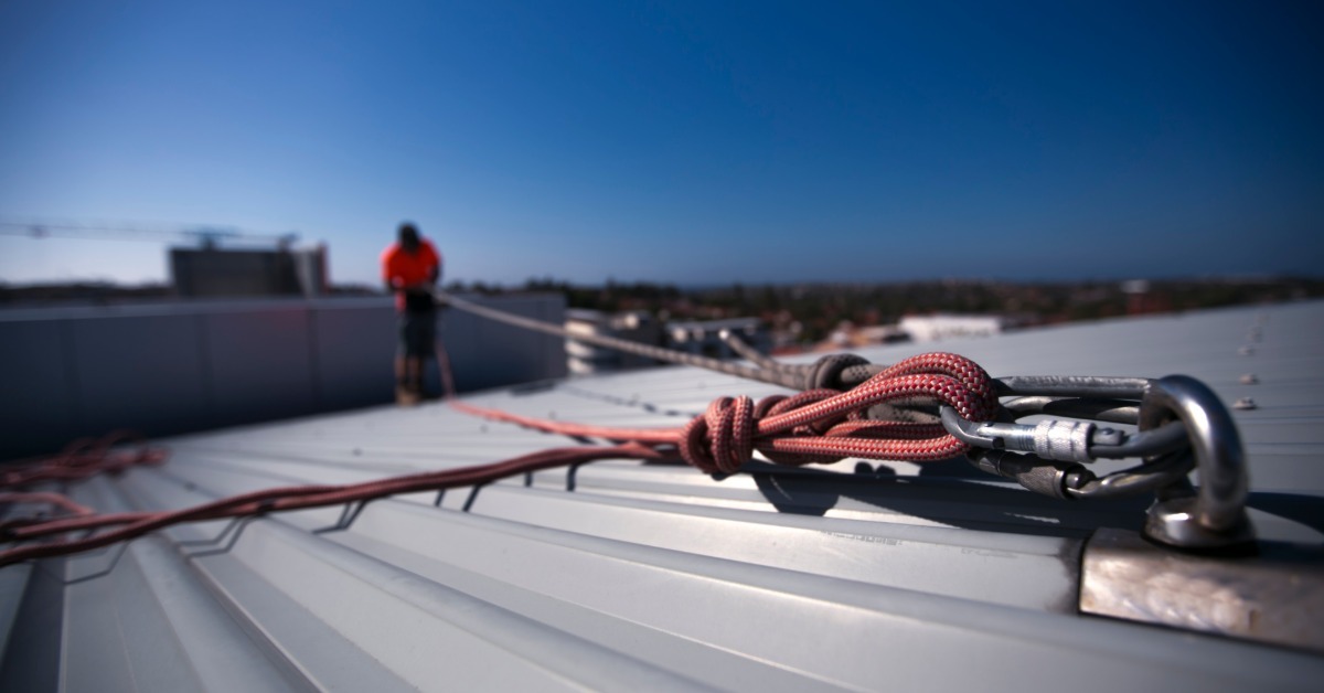 A close-up of an anchor point on a metal roof. There are carabiners containing multiple ropes connected to the anchor.